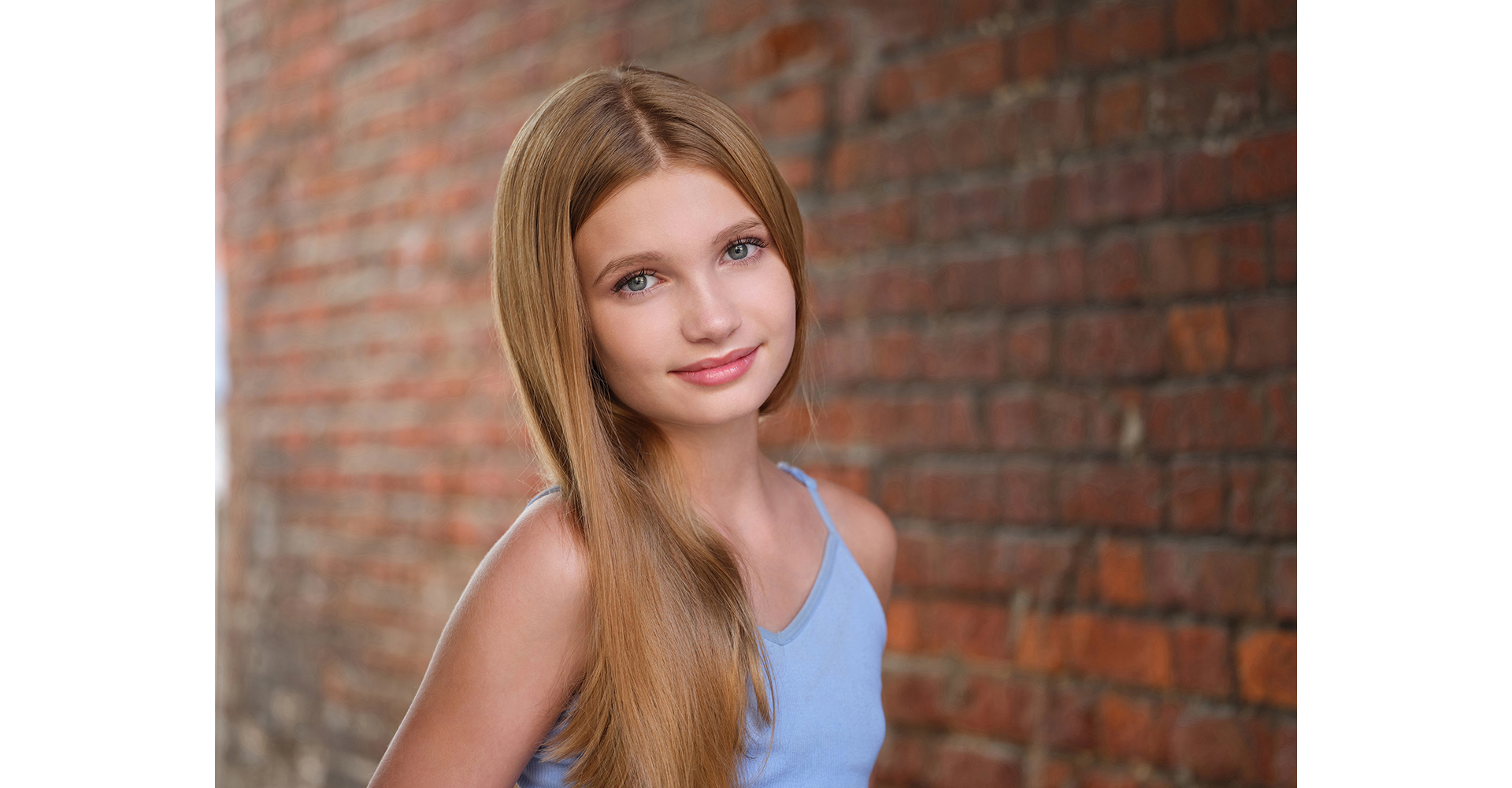 actress brown hair standing front of brick wall wearing black top head shot natural light